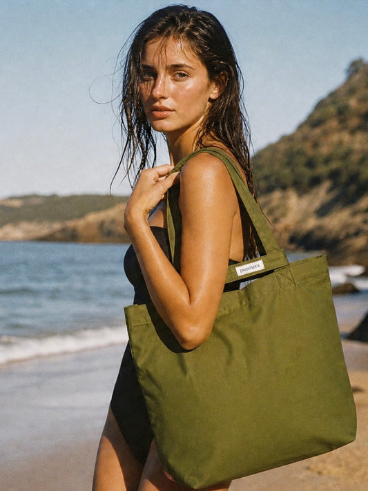 Woman holding a green tote bag on a beach with mountains in the background