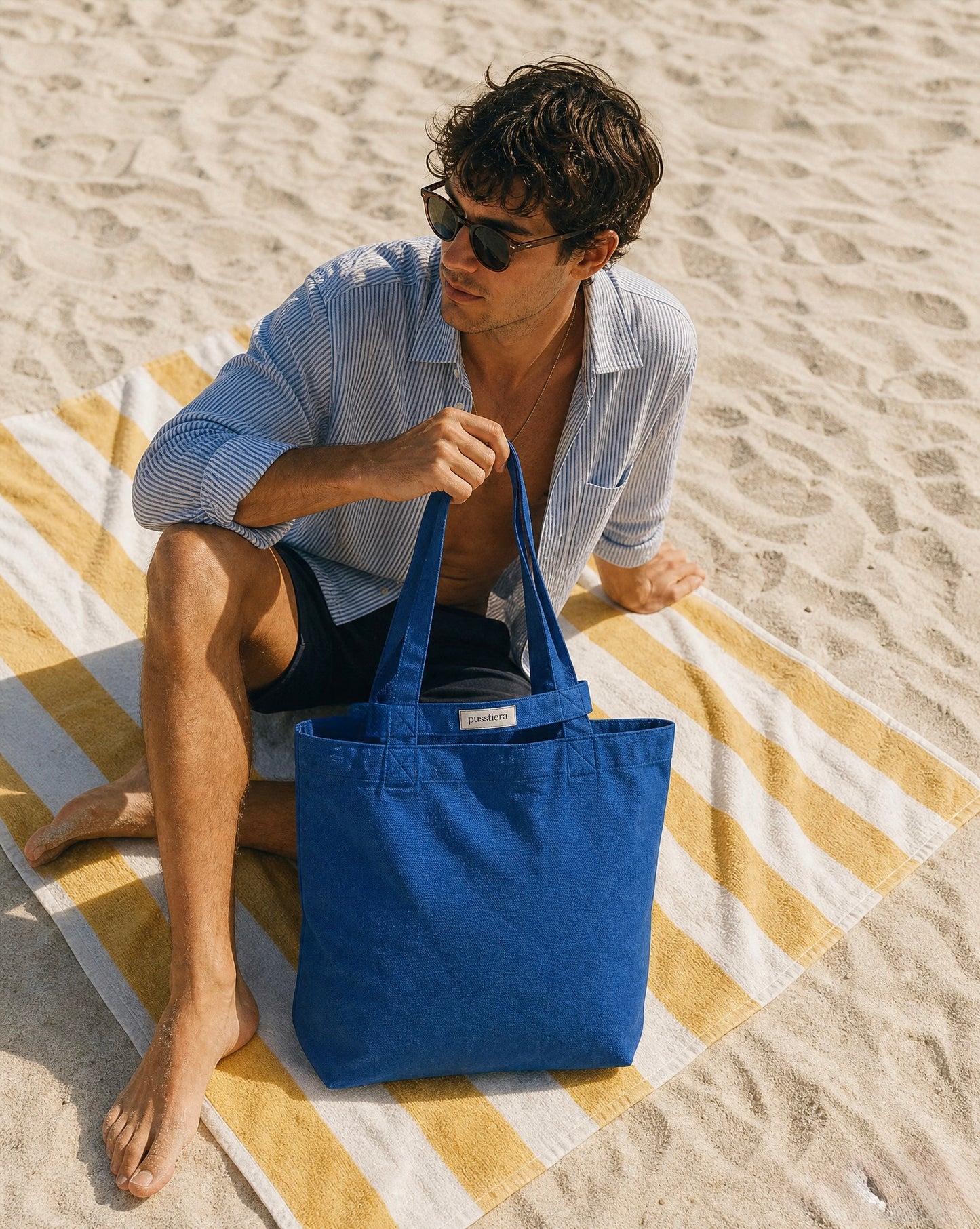 Man sitting on a beach with a blue tote bag